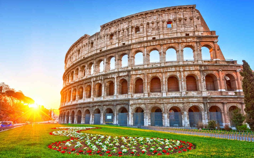 A view of the Roman Colosseum at sunrise with a manicured garden and colorful flowers in the foreground.