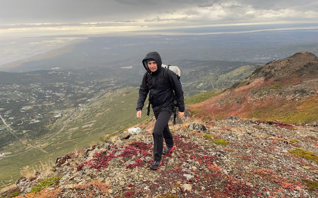 A man hikes uphill with a coastal view behind him.