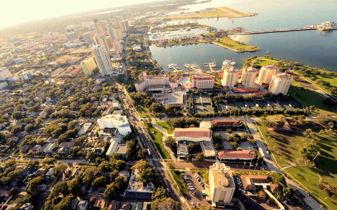 Aerial view of a coastal city with a mix of high-rise buildings, residential areas, and green spaces, along with a marina and water bodies in the background.